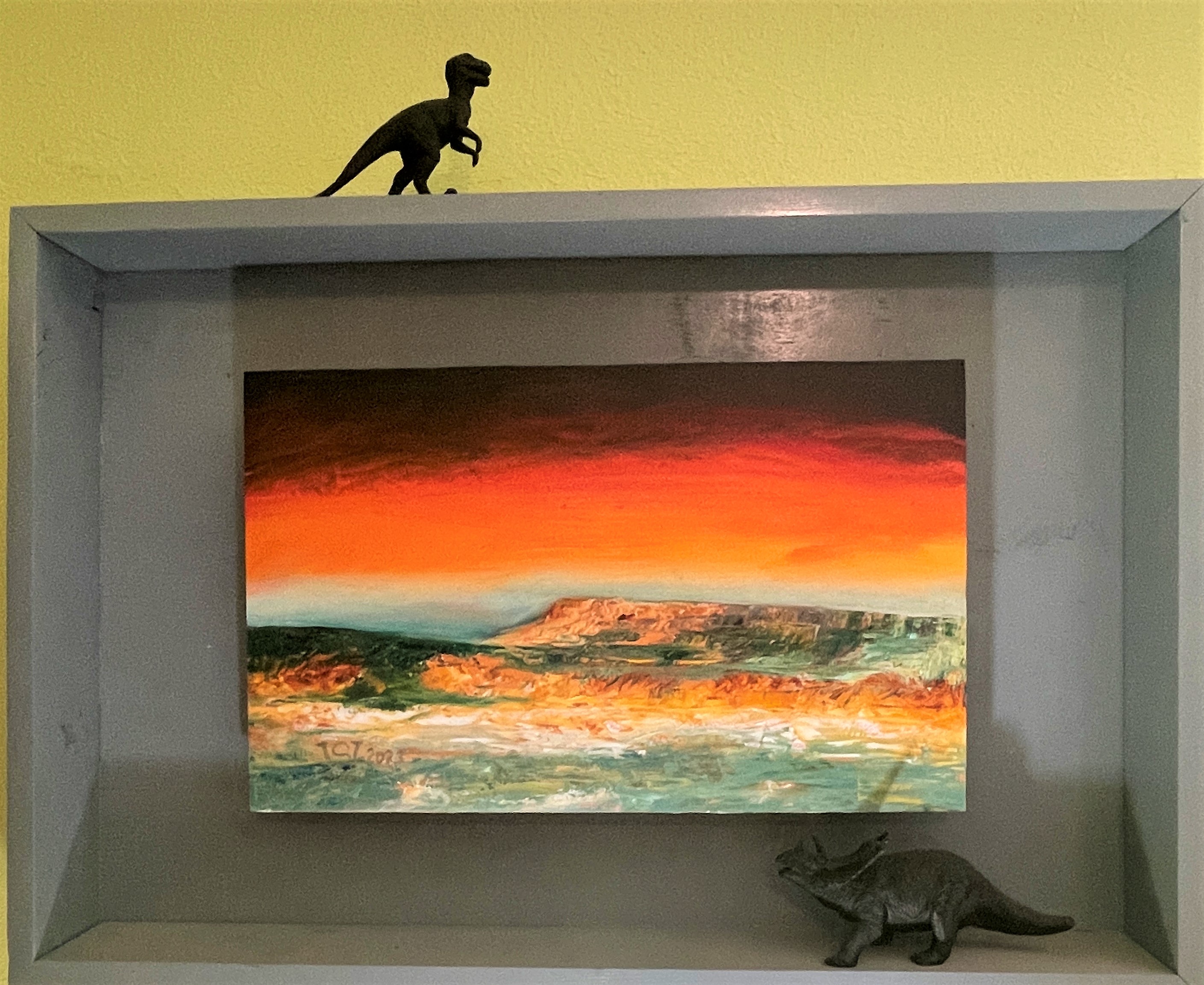 painting of desert mesas with red sky in a diorama with plastic dinosaur figurines in the fame